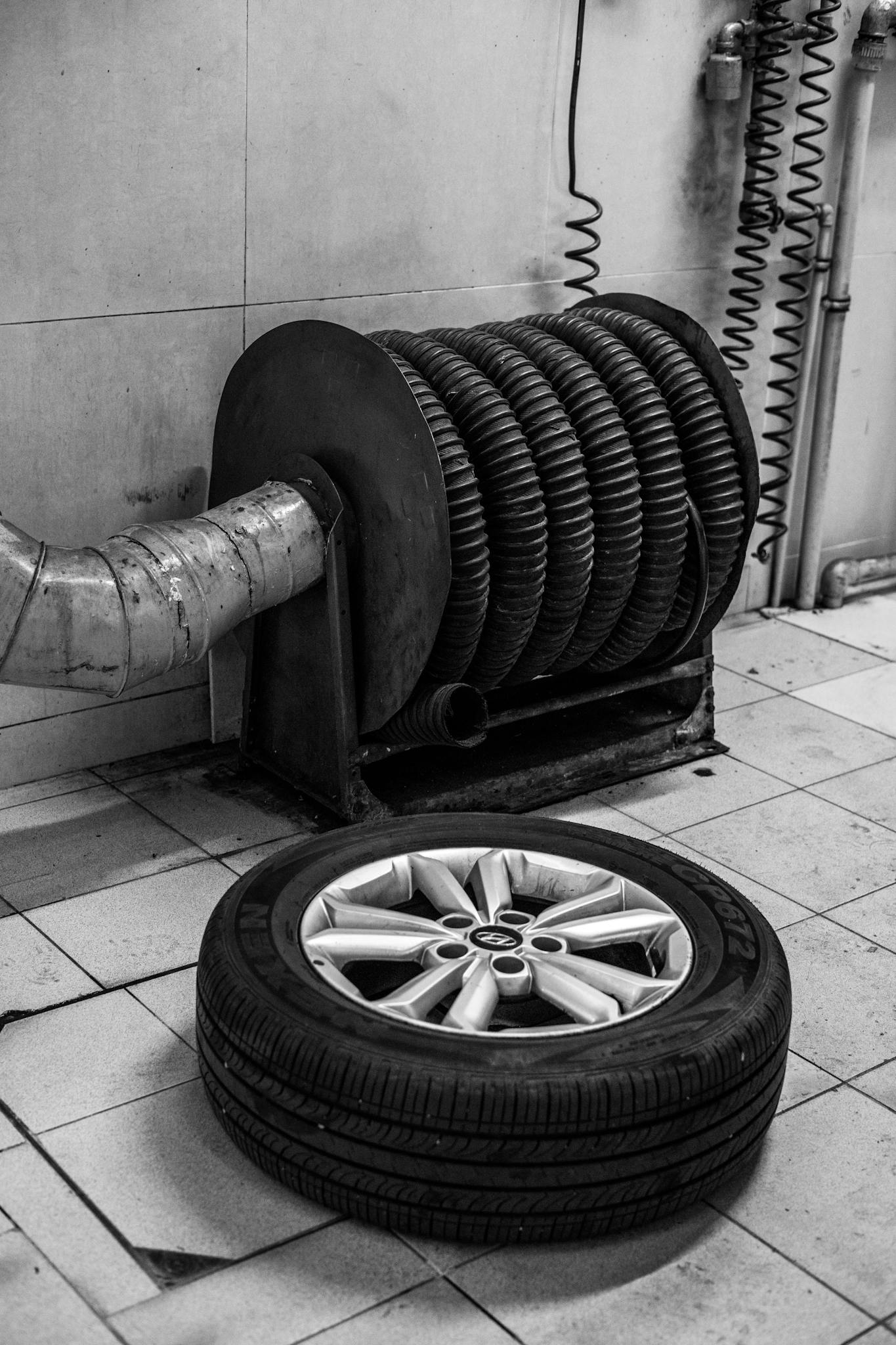 A black and white photo of a tire on the floor of a car repair shop next to equipment.