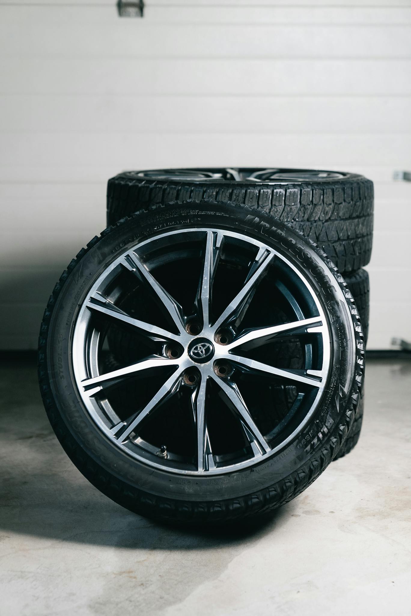 Close-up of stacked car tires and alloy wheels in a garage setting, showcasing automotive equipment.
