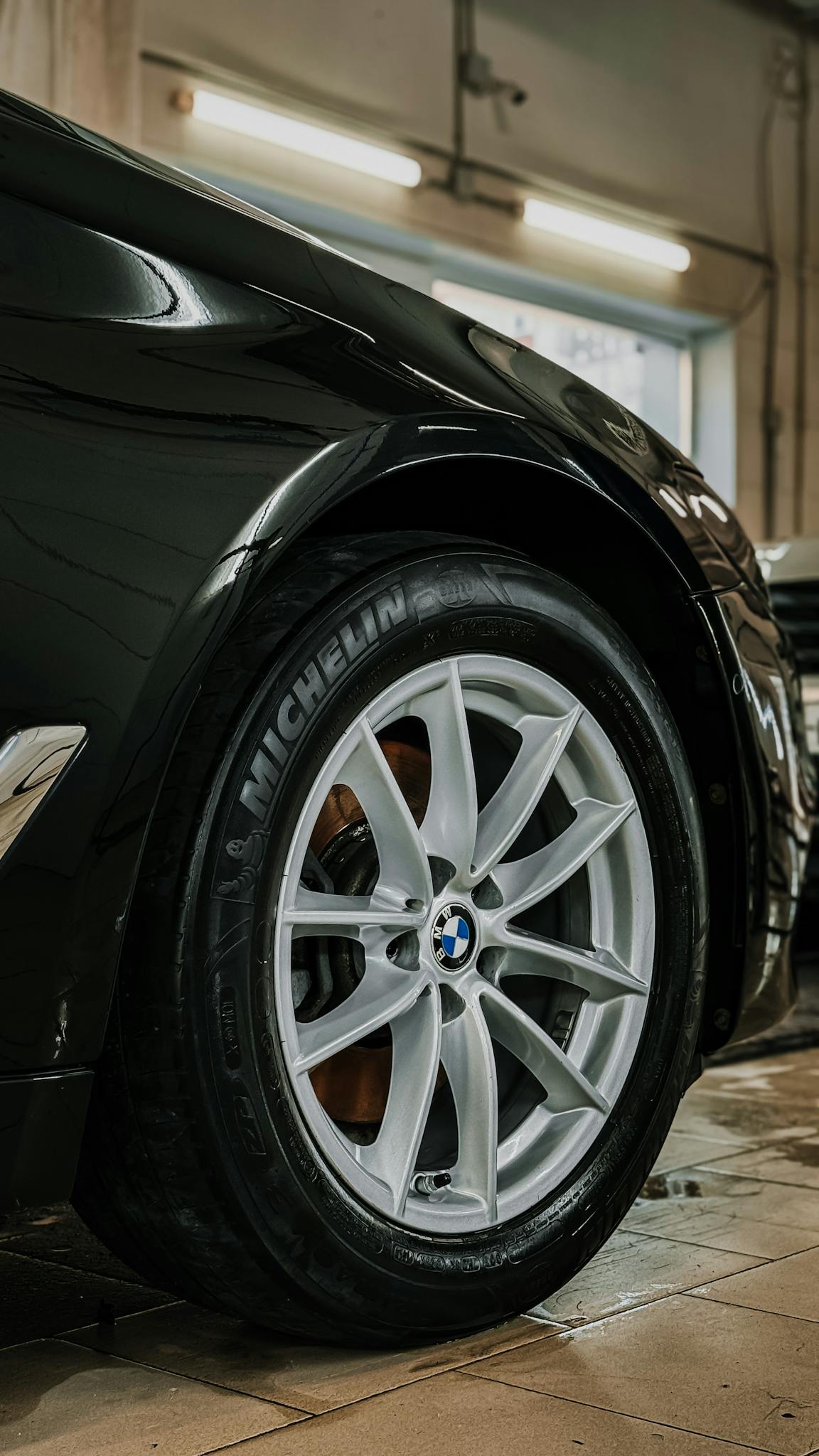 Detailed view of a luxury car wheel in a garage setting, highlighting tire and rim design.